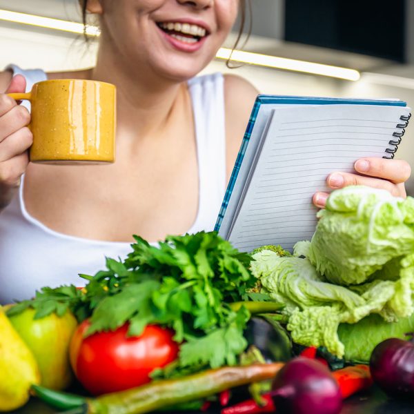 A young woman in the kitchen with a notepad among vegetables, the concept of cooking, dieting and healthy eating.